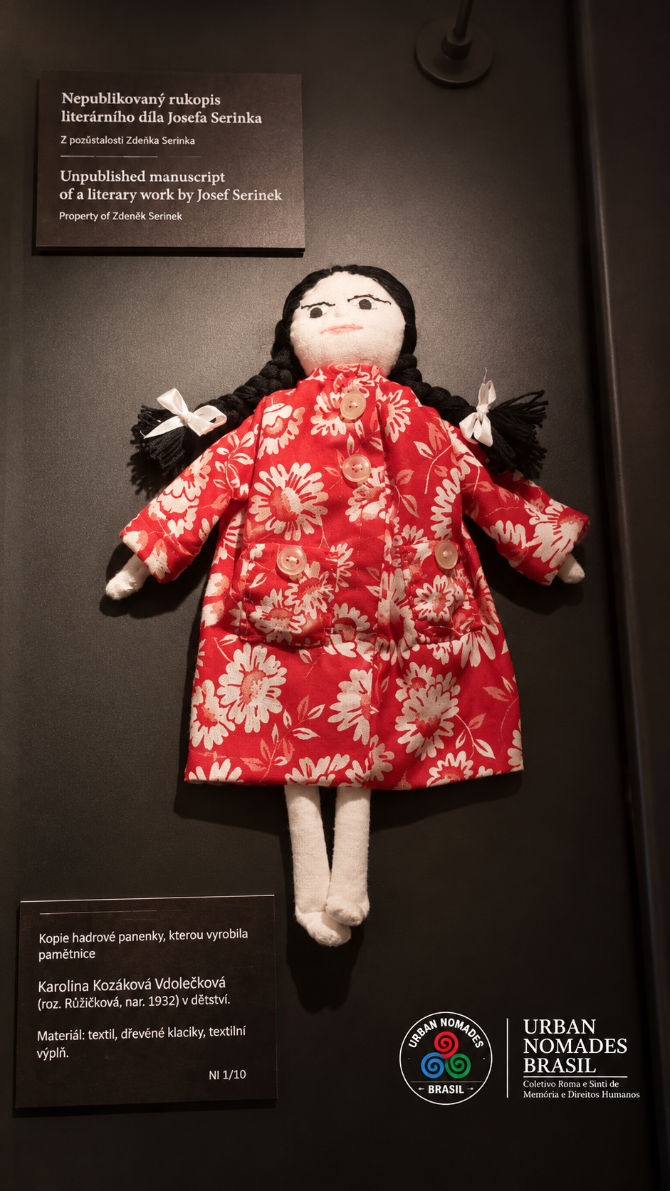 Réplica de boneca de pano com vestido vermelho florido, exposta em museu na República Tcheca